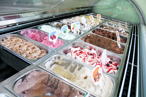 Ice cream fridge with creamy and fruit Italian ice cream steel serving counter with many of refreshing sweet scoopable flavors. Ice cream display, various flavors of gelato ice cream. Pastry shop.