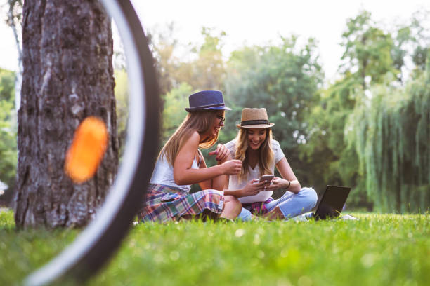 istock Two young women students in park sitting on grass talking, using laptop 1031023850
