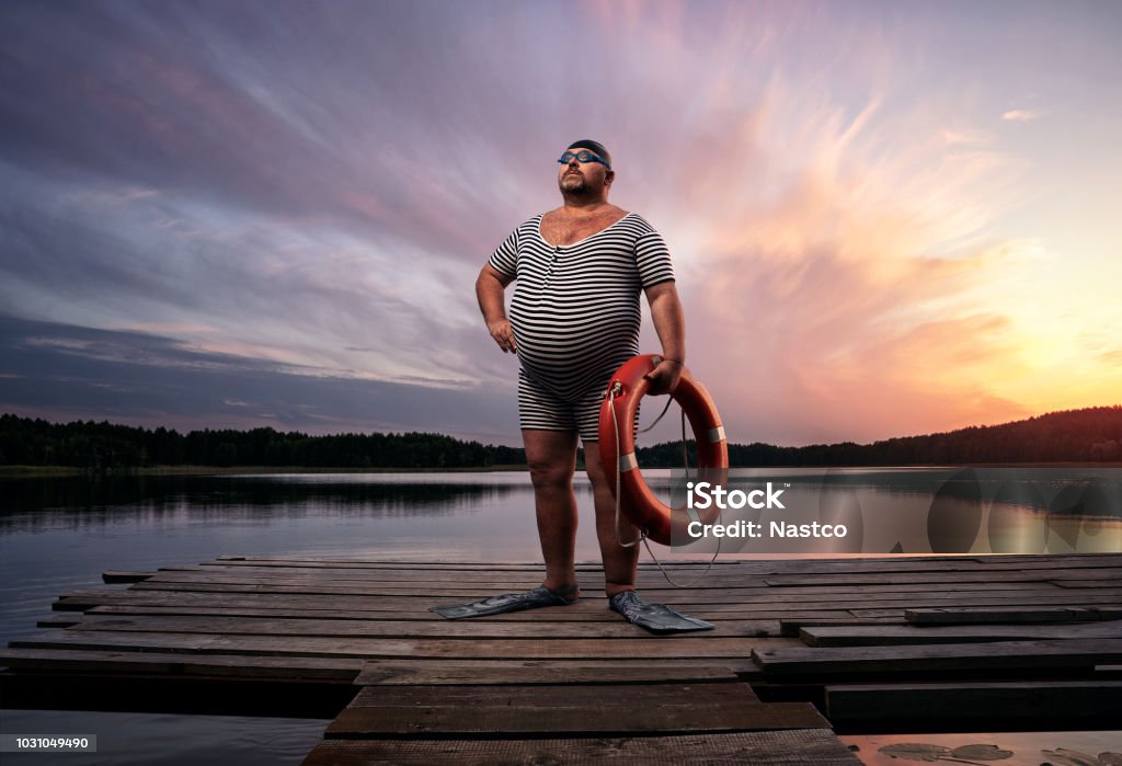 Funny retro swimmer Fuunny overweight, retro swimmer by the lake, at the sunset with copy space Humor Stock Photo