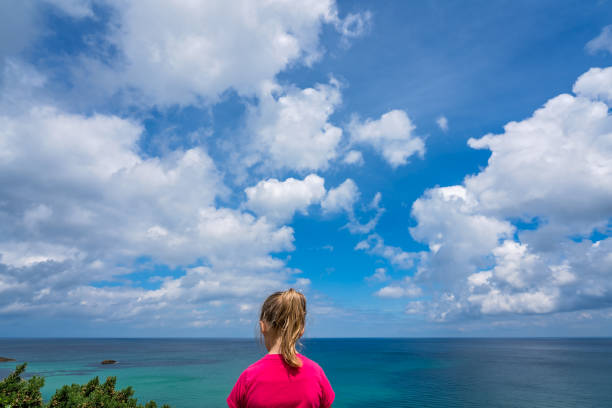 Little girl dressed in red t-shirt standing on a small cliff and admiting stunning Cornish coastline near St. Ives in Cornwall, England, UK
