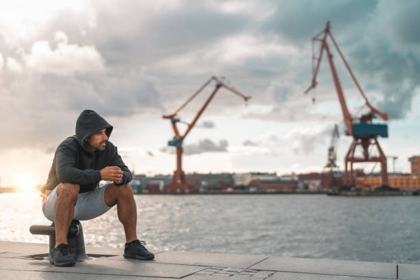A mature man is resting with a bottle of water in Gothenburg harbor after an outdoor exercise. Shot on a partly cloudy summer day in Sweden.