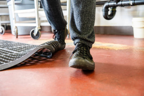 A man trips in a commercial kitchen. Trips, slips and falls in commercial kitchens are a major contributor to injuries sustained in the workplace. A food service worker tripping on a curled up floor mat. unsafe workplace stock pictures, royalty-free photos & images