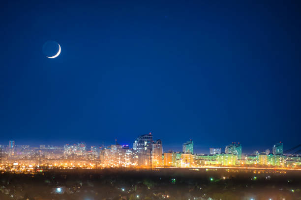 City at night with new moon on dark blue sky with stars
