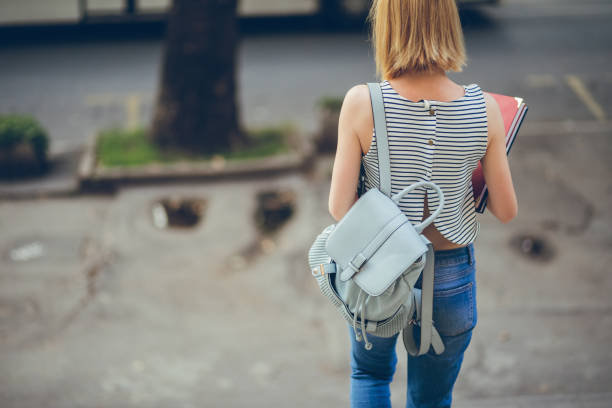 Young woman with backpack and textbook going down a staircase