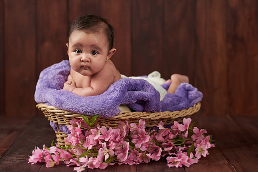 Baby girl lay in basket look to camera on dark wooden background
