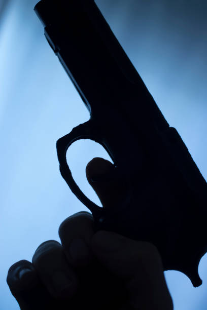 istock Pistol automatic handgun weapon in silhouette in hand of killer atmospheric dark dramatic photo. 1031112886