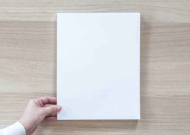 istock Blank A4 size book cover mockup template top view in businessman's hand with page front side on white surface flat lay on wood table 1031169708
