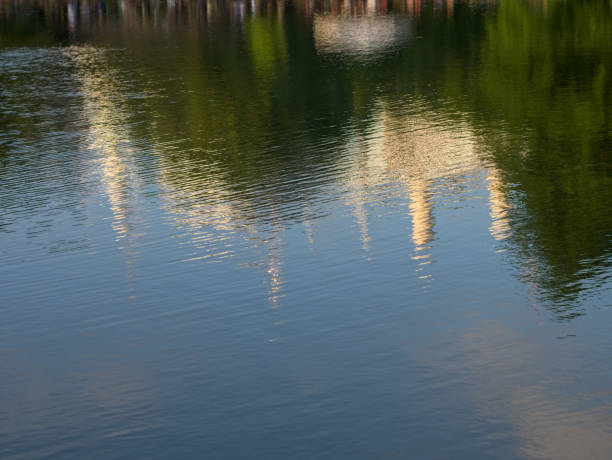 Reflection of white chimneys of a power plant, trees and blue sky on the water surface. Abstract background.