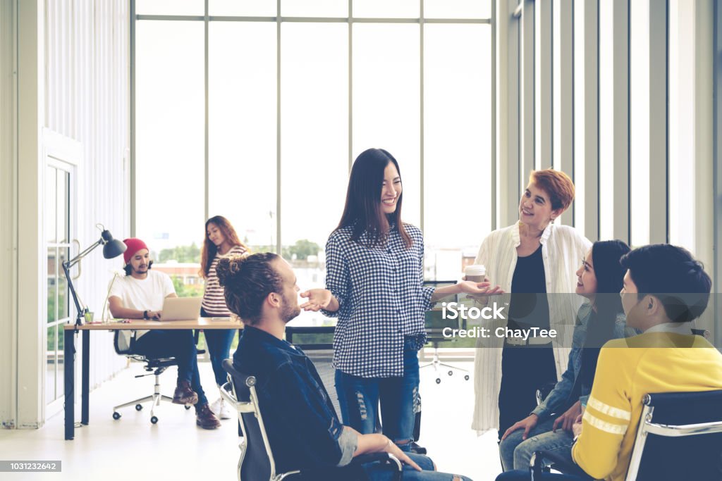 Group of young multiethnic creative team engaged brainstorm in small meeting while standing, sitting and talking together in modern office. Casual business with teamwork community discussion concept. Happiness Stock Photo