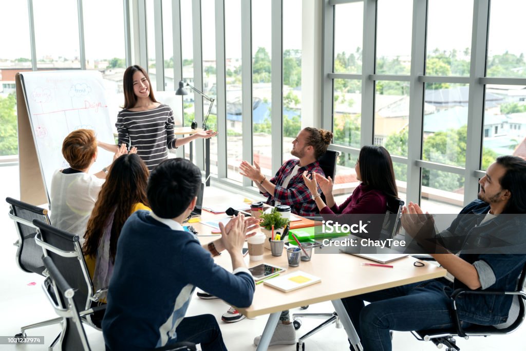 Joven empresaria asiática explicar idea al grupo de equipo creativo diverso de oficina moderna. Cargo contra la vista trasera del pueblo multiétnico. Altavoz aplausos de la audiencia después de la presentación. - Foto de stock de Clase de formación libre de derechos