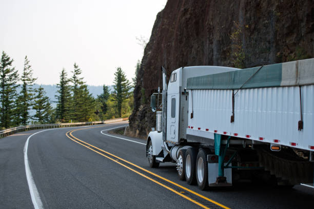 istock Big rig white semi truck with bulk covered semi trailer running around cliff wall on the curve road 1031238406