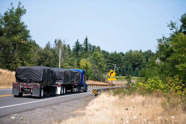 istock Blue big rig semi truck with two flat bed semi trailers transporting covered commercial cargo 1031240712