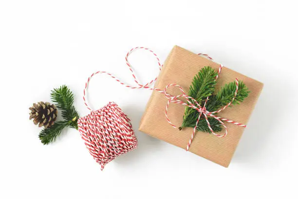 Christmas gift wrapped in craft brown paper and decorated with fir-tree branches isolated on whote background. New year gift giving concept.