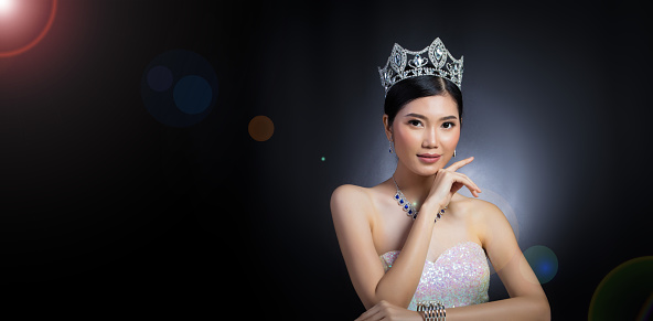 Portrait of Miss Pageant Beauty Contest in sequin Evening Ball Gown long dress with sparkle light Diamond Crown, Asian Woman fashion make up black hair style, studio lighting dark background dramatic