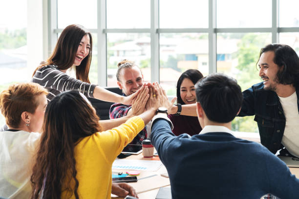 grupo de jóvenes diversos multiétnico gesto mano alta cinco, riendo y sonriendo juntos en reunión brainstorm en oficina. negocios informal con concepto de celebración de comunidad de trabajo en equipo de inicio. - spanish and portuguese ethnicity fotos fotografías e imágenes de stock