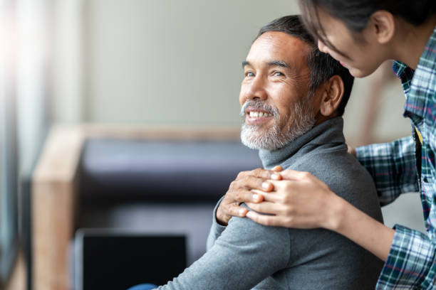 smiling happy older asian father with stylish short beard touching daughter's hand on shoulder looking and talking together with love and care. family relationship with bond and care concept. - senior adult with daughter father imagens e fotografias de stock