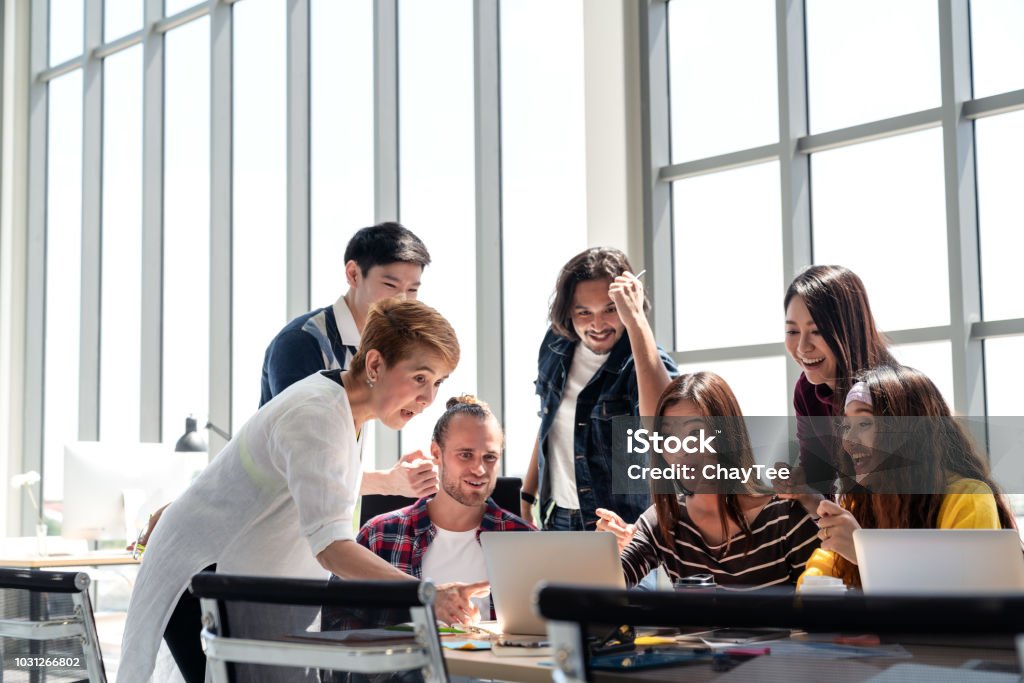 Group of Diversity People Team smiling and excited in success work with laptop at modern office. Creative Multiethnic or diverse teamwork feeling happy, enjoy and engaged with achievement project. Asian and Indian Ethnicities Stock Photo