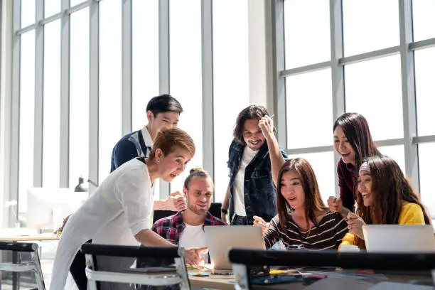 Group of Diversity People Team smiling and excited in success work with laptop at modern office. Creative Multiethnic or diverse teamwork feeling happy, enjoy and engaged with achievement project.