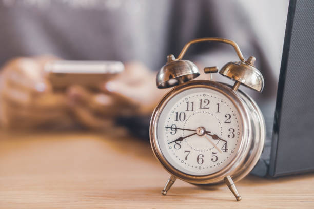 istock woman worker wasting time at work using smart phone with alarm clock on office desk 1031276114