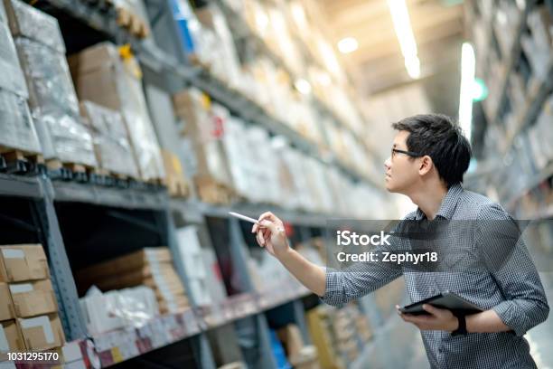 Young Asian Man Worker Doing Stocktaking Of Product In Cardboard Box On Shelves In Warehouse By Using Digital Tablet And Pen Physical Inventory Count Concept Stock Photo - Download Image Now