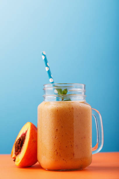 Smoothies made from ripe peaches. Healthy drink in a glass jar on a blue background stock photo