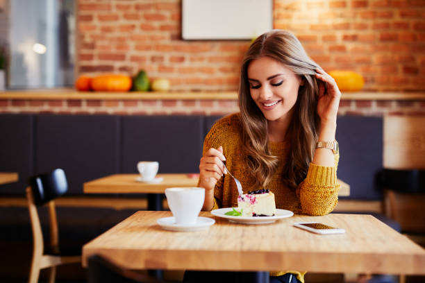 Gorgeous smiling woman eating cake and drinking coffee at a cafeteria