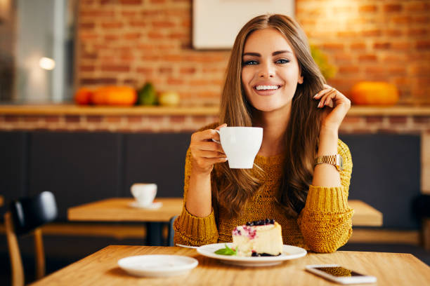 istock Gorgeous smiling young woman looking straight at camera while drinking coffee and eating cake in a cafe 1031312850