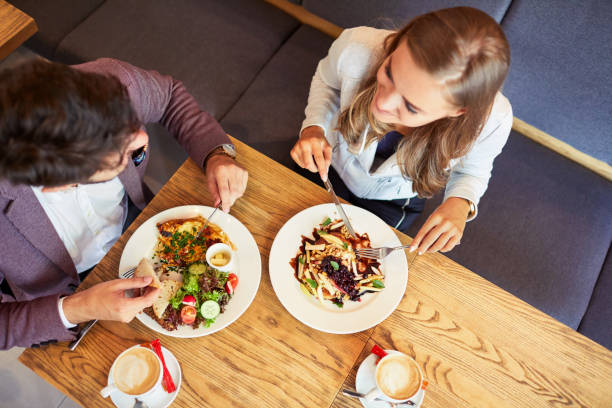 Couple of young people eating breakfast together while sitting in restaurant and smiling Couple of young people eating breakfast together while sitting in restaurant and smiling cafeteria photos stock pictures, royalty-free photos & images