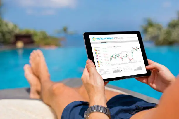 Photo of Man trading digital currencies online while relaxing by the pool.