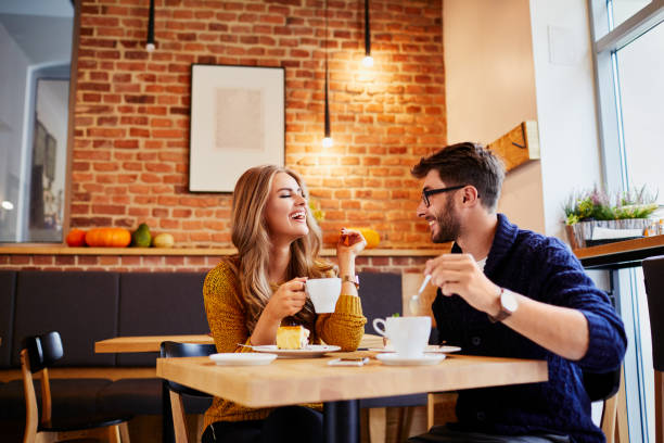 couple of young people drinking coffee and eating cake in a stylish modern cafeteria - coffee women friendship cafe imagens e fotografias de stock