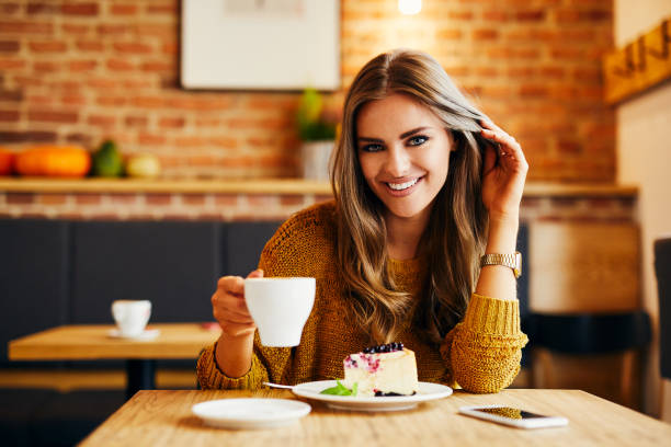 istock Portrait of a beautiful smiling young lady drinking coffee and looking at camera while sitting at table in a cafe 1031316810