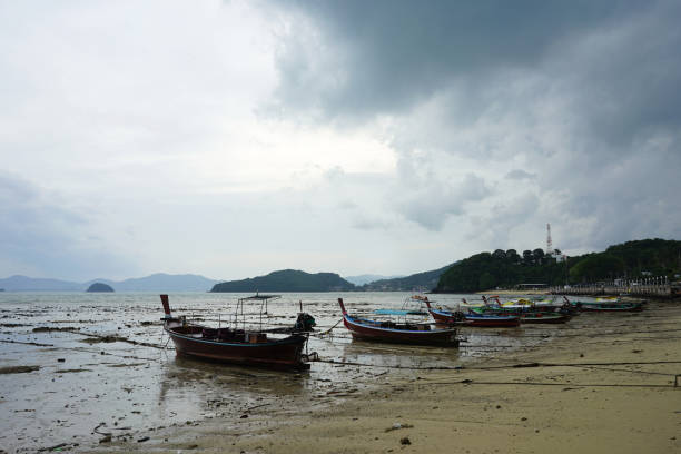 Fisherman boat parking on the lower tide beach with the dull sky background in Phuket