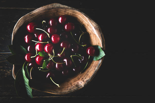 reife süßkirsche in holzschale auf dunklem hintergrund - black cherries stock-fotos und bilder