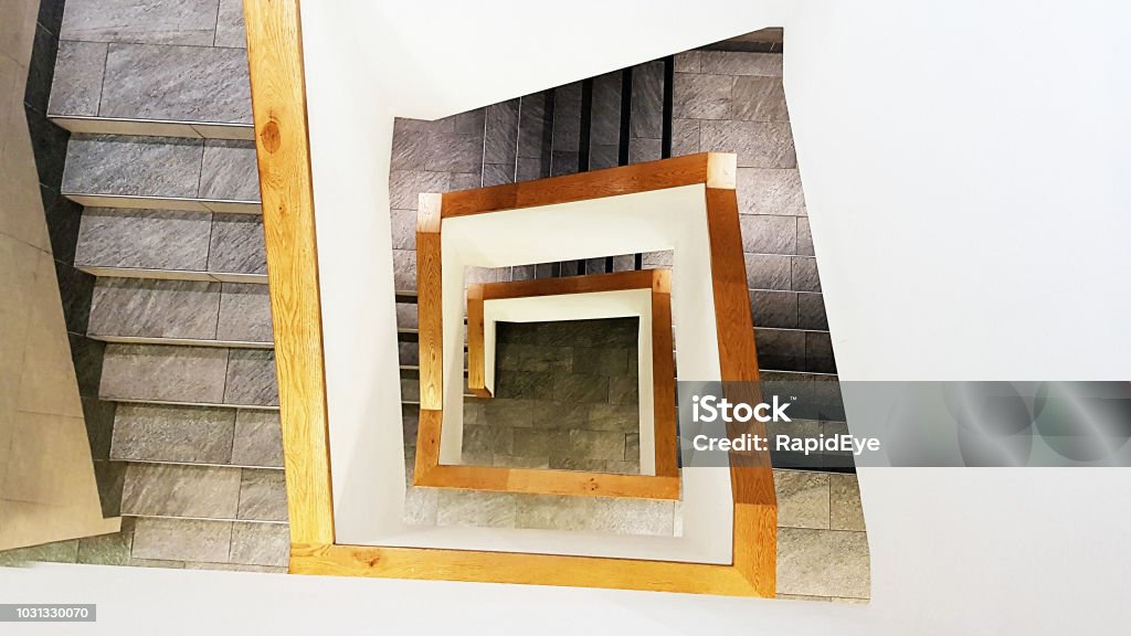 Abstract view down angular stone staircase Looking down on a spiral square staircase descending many stories, made of stone and metal. Abstract Stock Photo