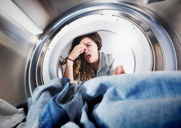 Young woman reaches into tumble drier, holding her nose, grimacing A lovely young woman grimaces, holding her nose as she reaches into a tumble dryer to remove some smelly laundry. Seen from inside the drier. holding nose stock pictures, royalty-free photos & images