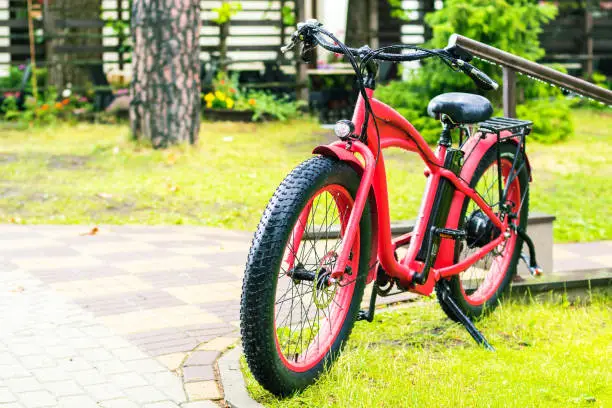 Red electrobicycle with wide tires standing on a green grass in rainy day
