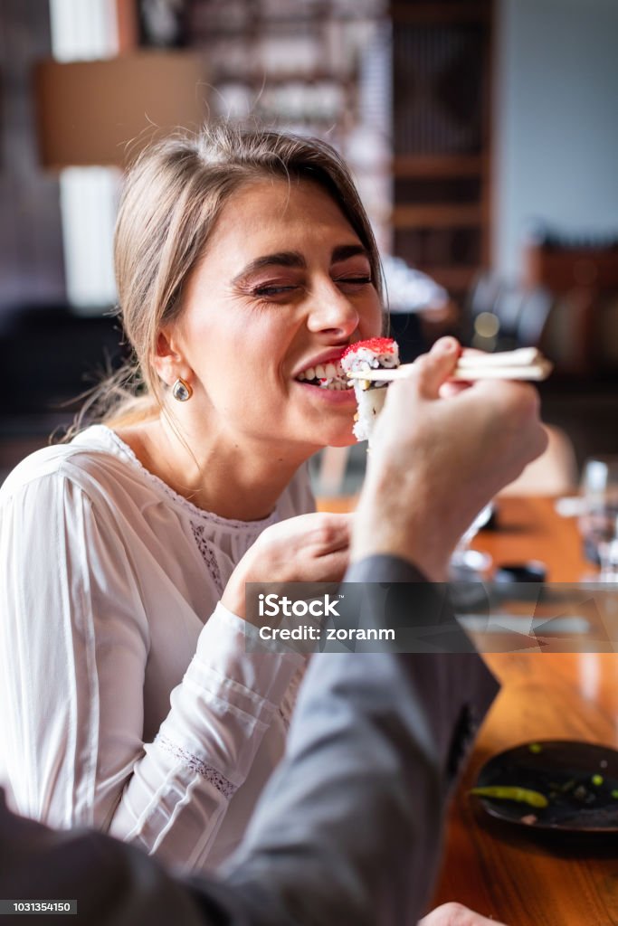 Woman taking a bite of sushi roll Businesswoman taking a bite of sushi roll held by colleague Sushi Stock Photo
