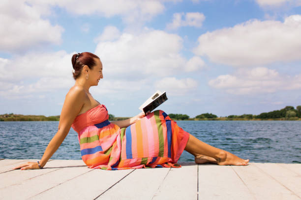 istock Smiling woman reading book on pier at the beach. 1031354826