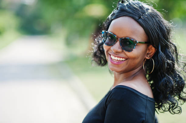 Close up portrait of smiling african american girl in sunglasses, black clothes posed outdoor. Fashionable black woman.