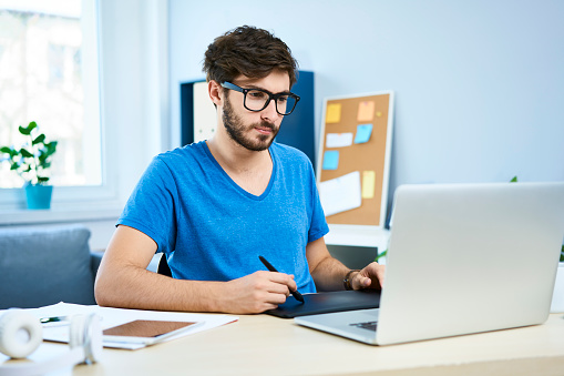 Thoughtful graphic designer working on laptop in home office