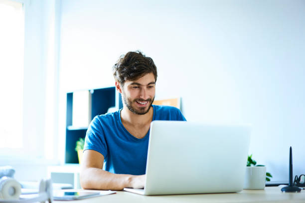 istock Smiling young man working on laptop in home office 1031361976
