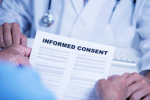 senior man reading an informed consent closeup of a senior caucasian man, at the doctors office, reading an informed consent document in front of a caucasian doctor man, in a white coat, sitting both at the doctors desk permission concept photos stock pictures, royalty-free photos & images