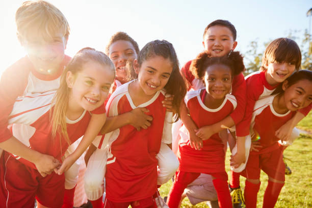 bambini alle elementari squadra sportiva piggybacking all'aperto - team sport foto e immagini stock