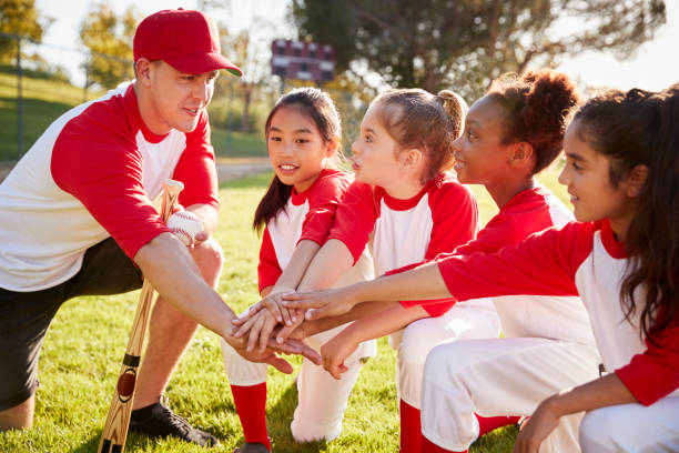 girl baseball team kneeling with their coach, touching hands - youth league imagens e fotografias de stock