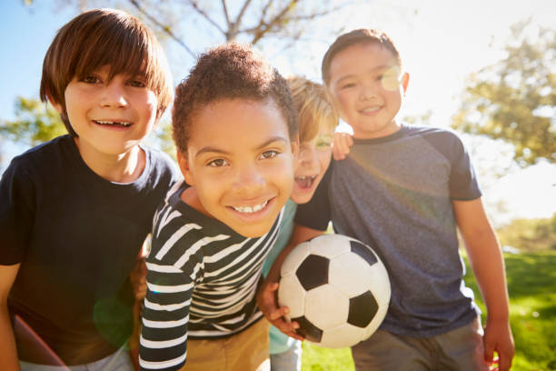 четверо молодых школьников, наклонившись к камере, держащей футбол - playing field sport friendship happiness стоковые фото и изображения