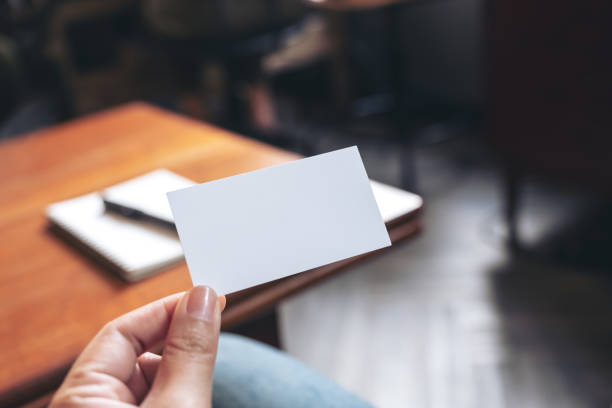 istock A hand holding white empty business card with notebook on wooden table 1031368974