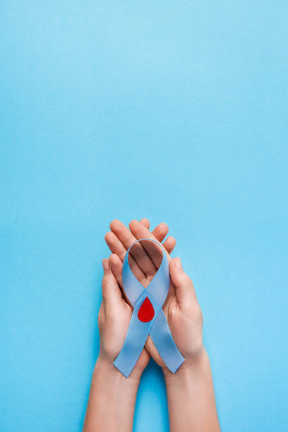 blue ribbon awareness with red blood drop in woman hands on a blue background, world diabetes day stock photo