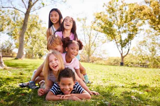 gruppo multietnico di bambini sdraiati in un mucchio in un parco - child playing multi ethnic group summer foto e immagini stock