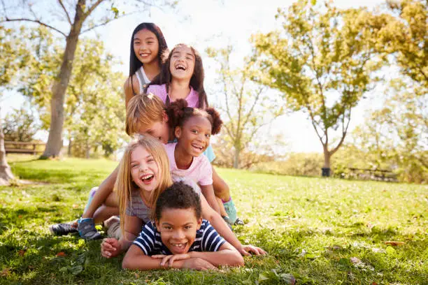 Photo of Multi-ethnic group of children lying in a pile in a park