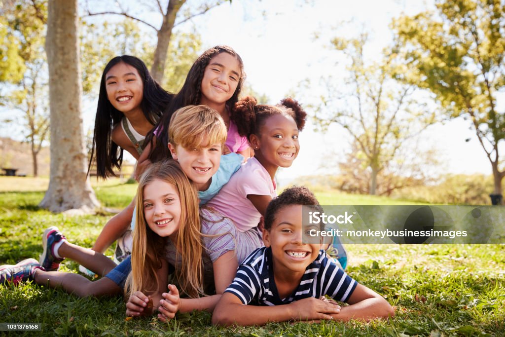 Gruppo multietnico di bambini sdraiati l'uno sull'altro in un parco - Foto stock royalty-free di Bambino